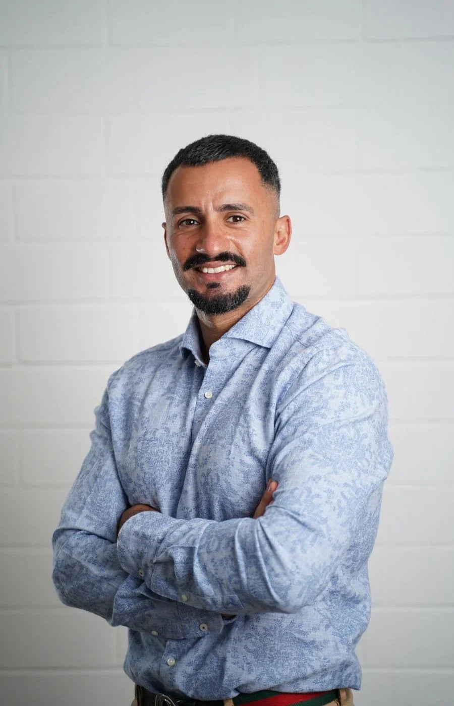 Ein Mann posiert freundlich mit angewinkelten Armen vor einer weißen Wand