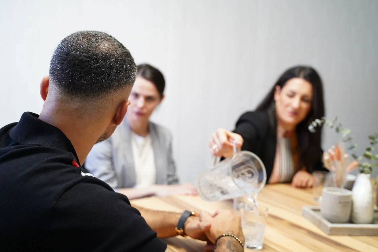 Drei Personen führen eine freundliche Besprechung am Tisch und schenken sich Wasser ein