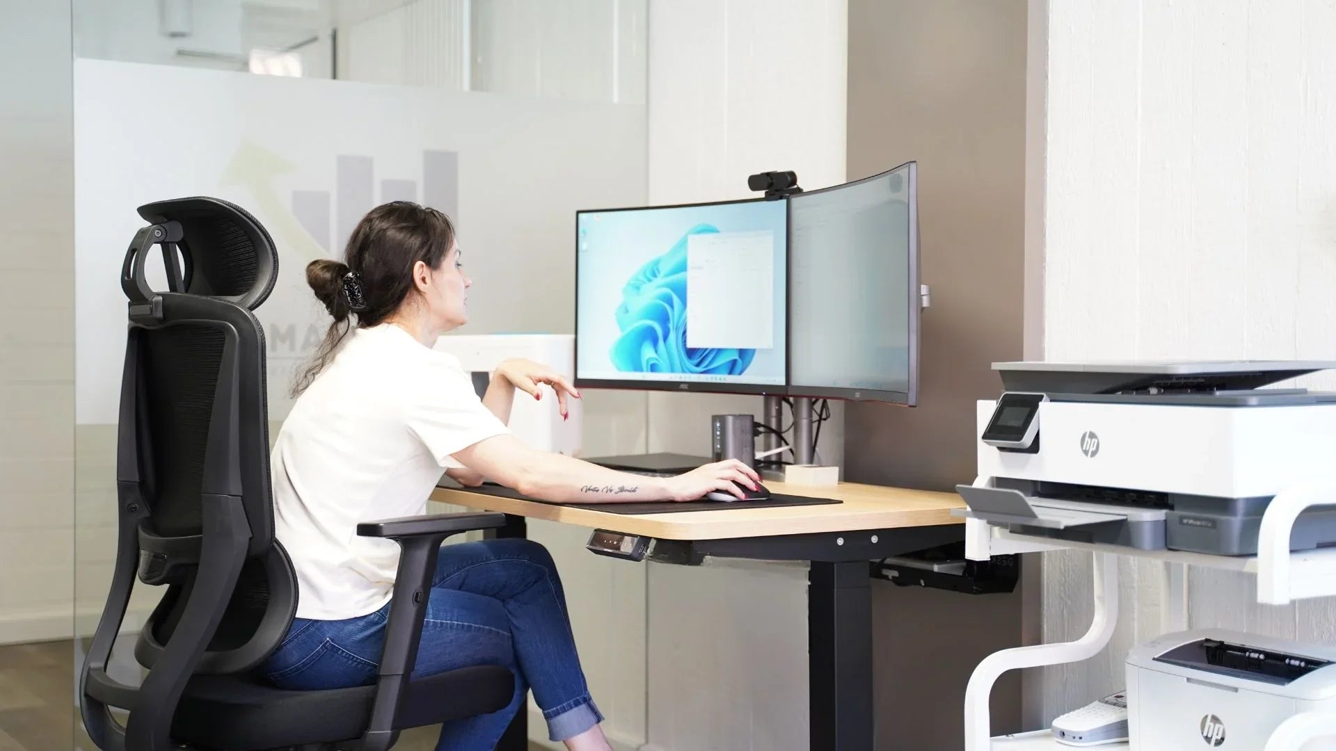 Dame sitzt fokussiert an ihrem ergonomischen Bürotisch in einem lichtdurchflutetem Raum