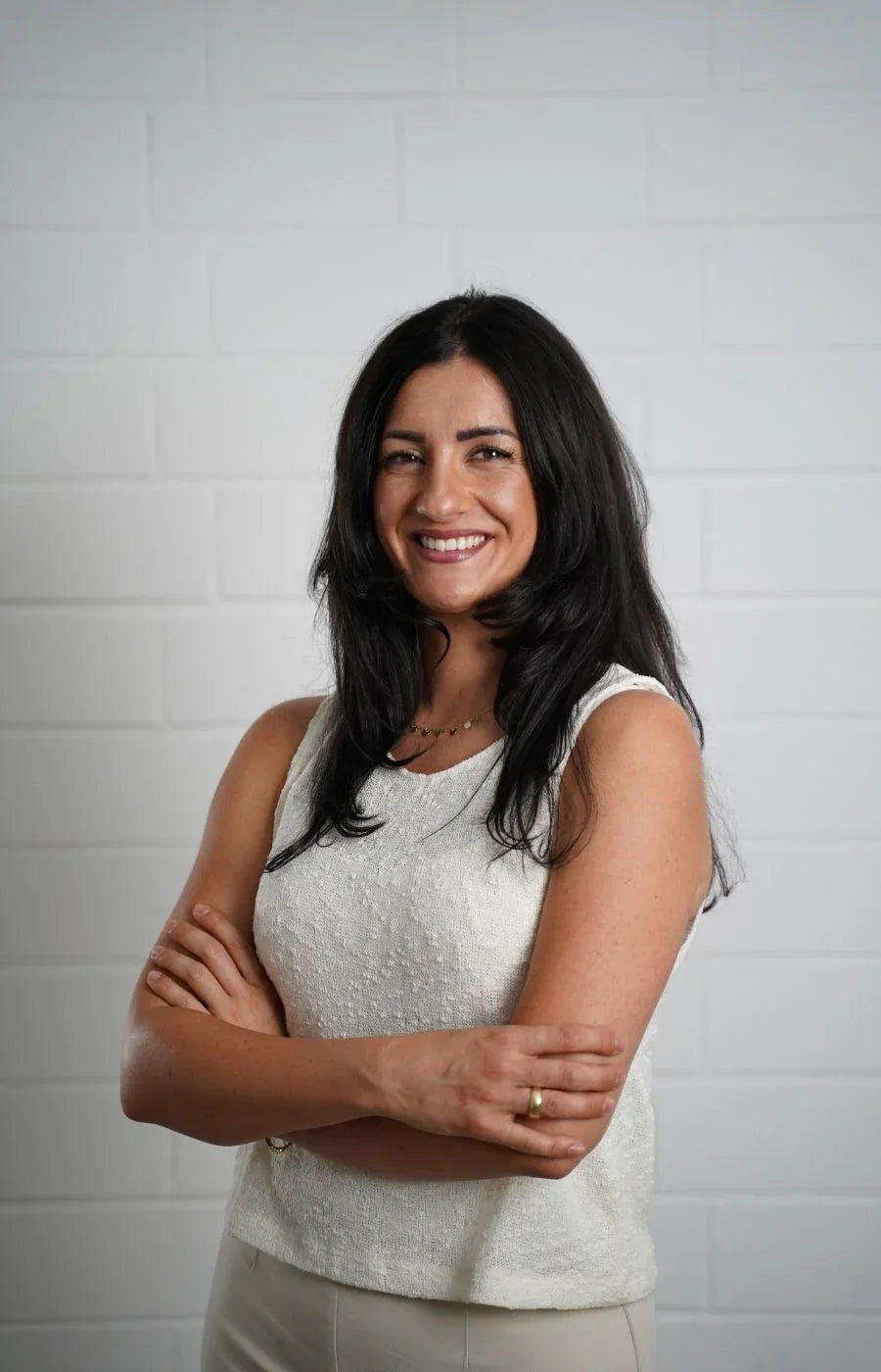 Eine Frau posiert freundlich mit angewinkelten Armen vor einer weißen Wand