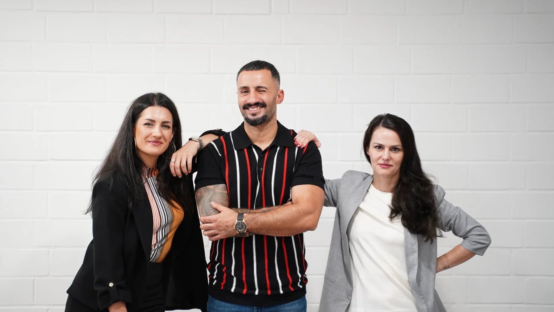 Drei Personen posieren vor einer weißen Wand für ein Teamfoto, mit freundlichem Lächeln