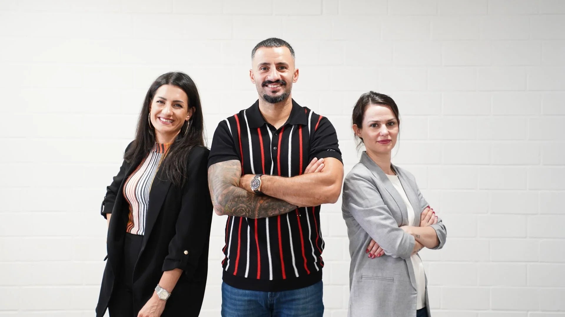 Drei Personen posieren vor einer weißen Wand mit angewinkelten Armen, für ein Teamfoto