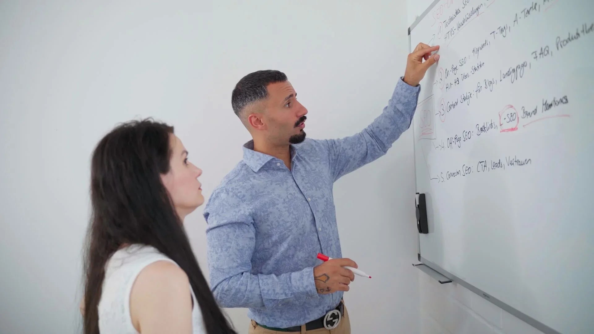 Zwei Personen stehen am Whiteboard und besprechen wichtige Punkte, in einem hellen Raum