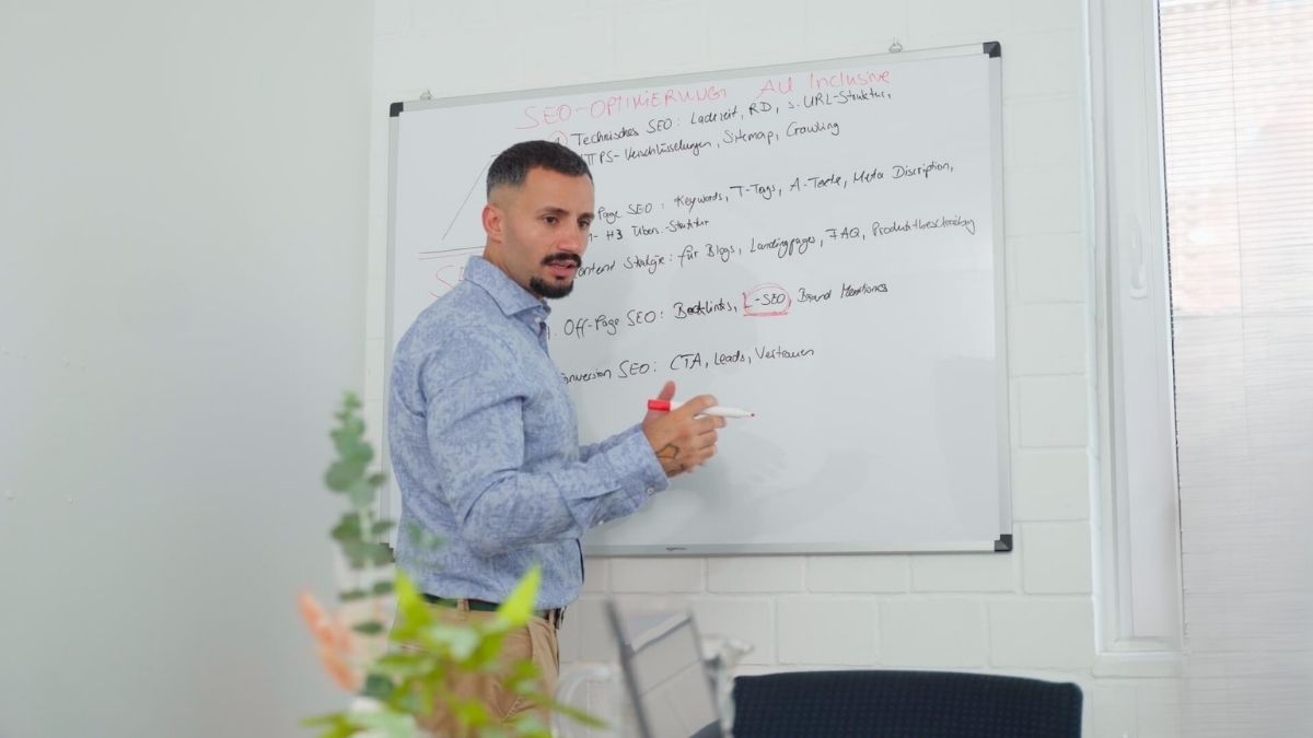 Mann steht am Whiteboard und lehrt andere Personen, in einem hellen Konferenzraum